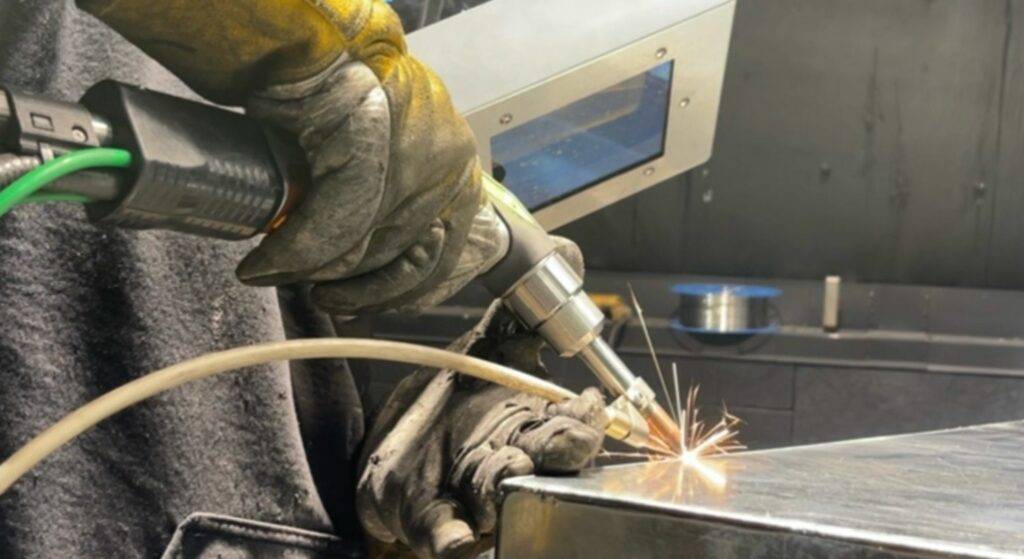 man laser welding a piece of metal with welding helmet on